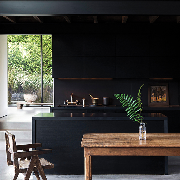 Modern farmhouse kitchen with black stained walls, cabinets and countertop with rustic natural farm table as a centerpiece. 